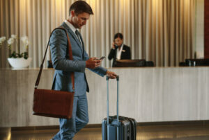 Young businessman walking in hotel lobby and using mobile phone. Business traveler arriving at his hotel.